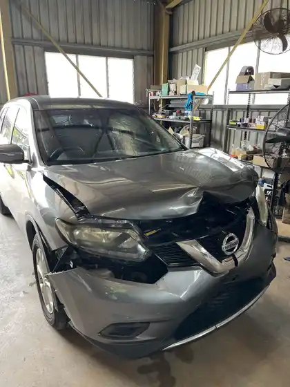 Front corner of a grey Nissan X-Trail after an impact, with a crumpled bonnet, split bumper and displaced grille